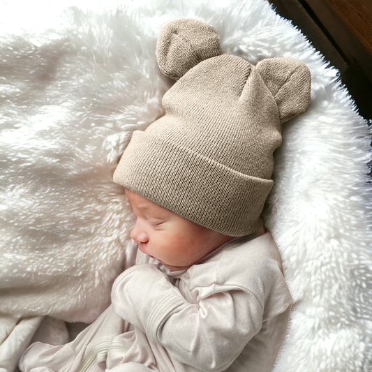 Newborn baby wearing a beige knit hat with bear ears on a soft white surface